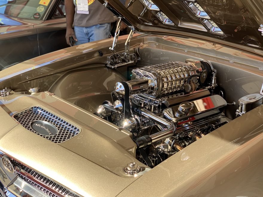 Motor com blower cromado sob o capô de um clássico dourado